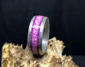 May include: A silver ring with a pink and purple glitter inlay. The ring is sitting on a piece of wood.