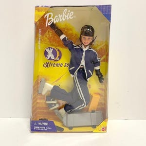 May include: Barbie Xtreme 360 Special Edition doll in packaging. The doll is wearing a blue and white athletic outfit, a black helmet, and protective gear. The doll is posed on a skateboard. The packaging has the Barbie logo.