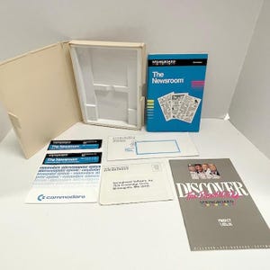 May include: An open beige box with a molded interior, a blue "The Newsroom" book, and various Springboard software materials. Includes Commodore labels and a "Discover Springboard" catalog.