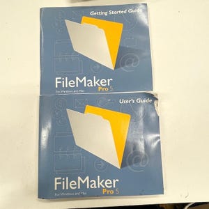 May include: Two FileMaker Pro 5 guides. The blue covers feature a white folder graphic with a yellow interior. The top guide is labeled "Getting Started Guide." The bottom guide is labeled "User's Guide." Both guides are for Windows and Mac.