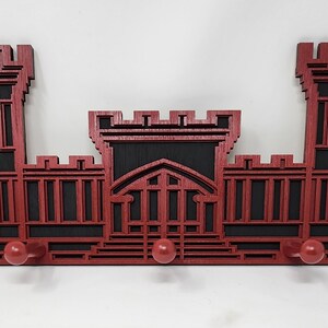 May include: Red wooden wall-mounted coat rack shaped like a castle with five hooks.