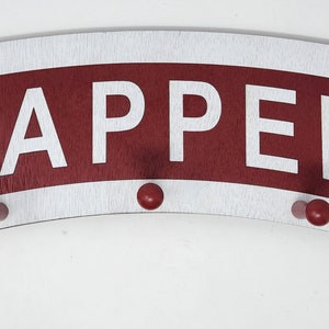 May include: A white wooden coat rack with a red curved sign that says "SAPPER" in white letters. The rack has five red wooden hooks.