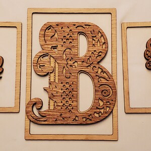 May include: Three wooden framed wall decor pieces featuring the letters A, B, and C. Each letter is intricately designed with a floral pattern and a woodgrain finish.