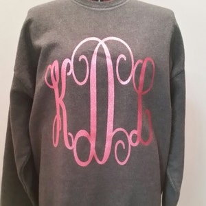 May include: A dark gray sweatshirt with a pink monogram of the letters "KLC" on the front.