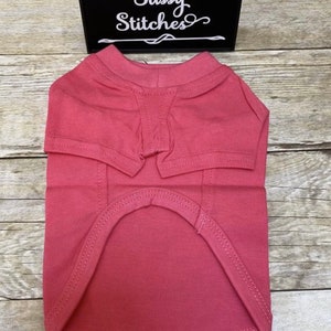 May include: A plain pink dog t-shirt with a crew neck and a  "Sassy Stitches" logo on the tag.