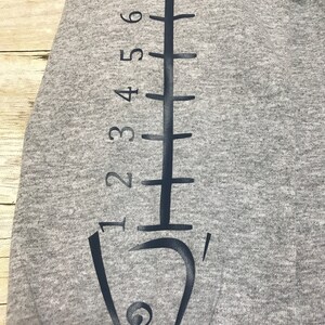 May include: Gray sweatshirt with a black fish outline and a ruler printed on the sleeve. The ruler is marked with numbers 1 through 8.
