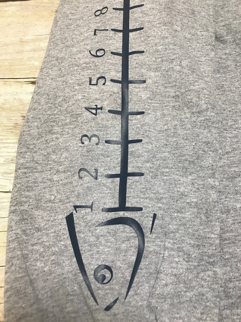May include: Gray sweatshirt with a black fish outline and a ruler printed on the sleeve. The ruler is marked with numbers 1 through 8.