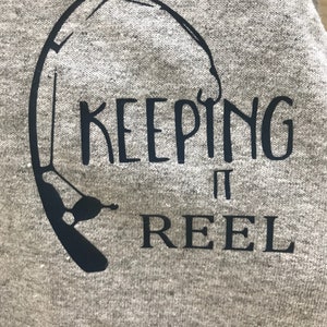 May include: A gray sweatshirt with a black graphic of a fishing rod and the text "KEEPING IT REEL".