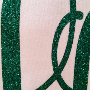 May include: Close-up of a green glitter "Peace" sign on a white background.