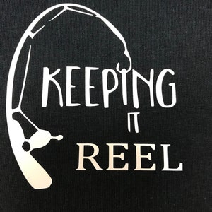 May include: Black t-shirt with a white graphic of a fishing rod and the text "KEEPING IT REEL".