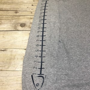 May include: Gray long-sleeve shirt with a black fish design on the sleeve. The fish design includes a scale pattern and numbers 1 through 18.