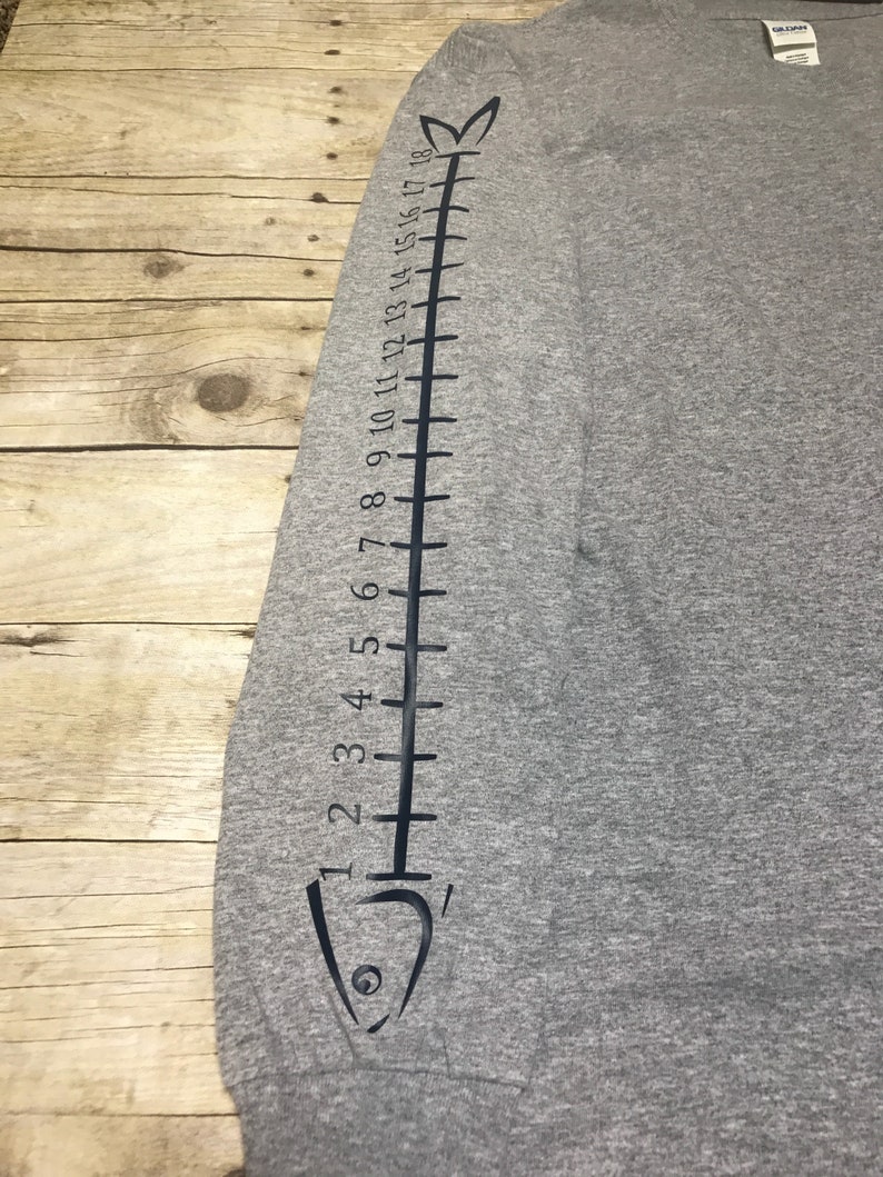 May include: Gray long-sleeve shirt with a black fish design on the sleeve. The fish design includes a scale pattern and numbers 1 through 18.