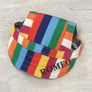 Puede incluir: Un gorro de perro a rayas de colores con el nombre "ROMEO" bordado en la parte delantera.