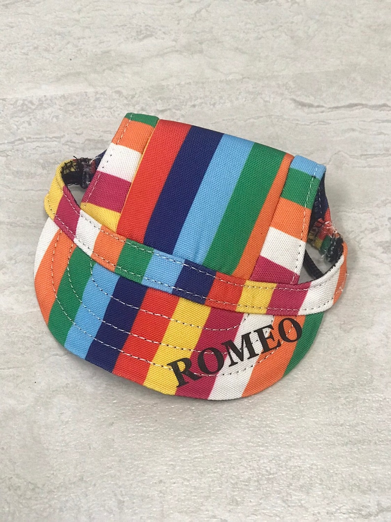 Puede incluir: Un gorro de perro a rayas de colores con el nombre "ROMEO" bordado en la parte delantera.