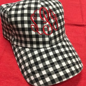 May include: A black and white gingham baseball cap with a red embroidered monogram. The monogram is a cursive "L.G."