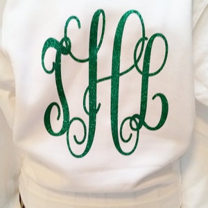 May include: White sweatshirt with a green glitter monogram "SLG" on the front. The sweatshirt is on a hanger and the text "Sassy Stitches" is visible on a black sign below.