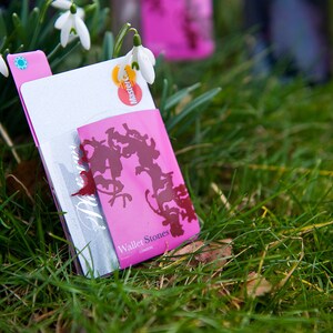 May include: A pink wallet with a white and silver card holder. The wallet features a design of stylised silhouettes of cats and the text "Wallet Stones" printed on the front.
