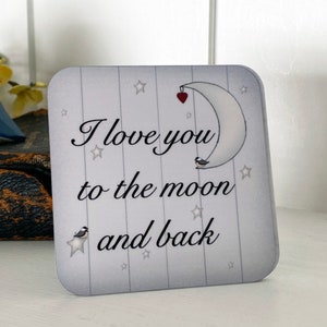 May include: A white and gray square coaster with a moon and stars design. The text "I love you to the moon and back" is printed on the coaster.