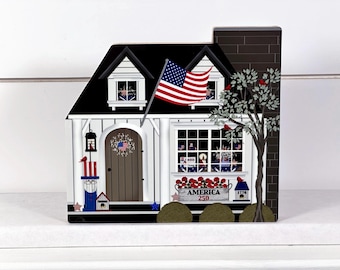 May include: A decorative wooden house with a black roof, white siding, and a brown door. An American flag waves from the roof. The house features a window box with the text "AMERICA 250" and a tree with red birds.