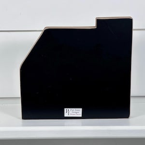 May include: A black wooden desk organizer with a unique angled design. The organizer has a rectangular base and a sloped side, with a small rectangular cutout at the top. The brand name "Pat Isaac Designs Home Decor" is printed on a white label.
