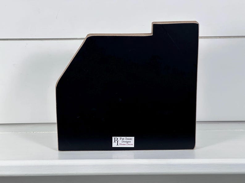 May include: A black wooden desk organizer with a unique angled design. The organizer has a rectangular base and a sloped side, with a small rectangular cutout at the top. The brand name "Pat Isaac Designs Home Decor" is printed on a white label.