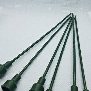 May include: A collection of six dark green floral stem picks. Each pick has a textured stem and a flared, cup-shaped head. The stems are approximately 6 inches long, and the heads have a jagged edge.