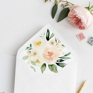 May include: A white envelope with a floral design on the flap. The design features a bouquet of white and pink flowers with green leaves. The envelope is lying flat on a white surface.