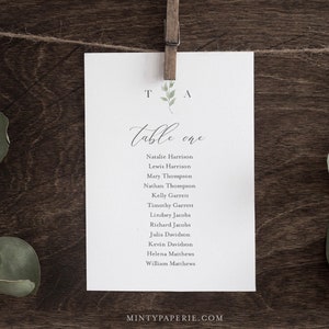 May include: A white card with a handwritten table number "Table one" and a list of names for a wedding reception. The card is attached to a string with a wooden clothespin.