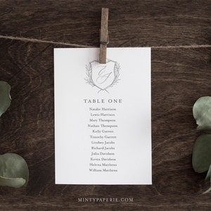 May include: A white card with a gray floral design and the text "TABLE ONE" printed on it. The card lists the names of guests for a wedding reception.