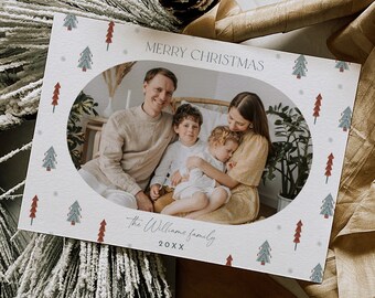 Può includere: Un biglietto di Natale con una foto di famiglia all'interno di una cornice ovale. Il biglietto ha uno sfondo bianco con un motivo di piccoli alberi di Natale e fiocchi di neve. Il testo "MERRY CHRISTMAS" è in alto, con "The Williams family" e l'anno in basso.