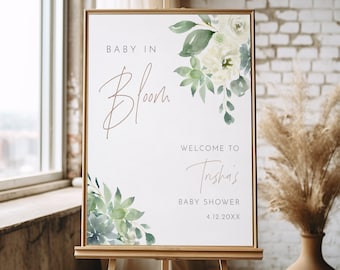 May include: A white sign with green watercolor floral designs and the text "Baby in Bloom" and "Welcome to Trisha's Baby Shower 4.12.20XX".
