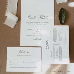 May include: Elegant wedding invitation suite with calligraphy script. The set includes a main invitation, response card, and details card. The design features minimalist typography and layout on white paper. A cream-colored ribbon and a green leaf accent the stationery.