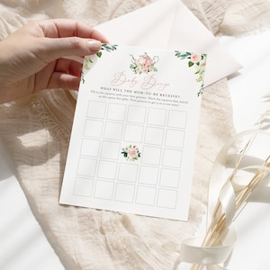 Puede incluir: Una tarjeta de juego de baby shower imprimible con un diseño floral y el texto "Baby Bingo" y "¿Qué recibirá la futura mamá?" Rellena los cuadrados con tus mejores conjeturas. Marca los cuadrados que coincidan a medida que abre sus regalos. ¡La primera persona en obtener 5 en fila gana!