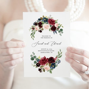 May include: Wedding invitation with a watercolor floral design in shades of burgundy, pink, and blue. The text reads "Welcome to the wedding of Jurk ul Eloul, August 23, 2019, Mountainville Manor, Middletown, NY".