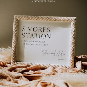 Puede incluir: Un cartel blanco con un marco de madera dice "S'mores Station" con el texto "Please help yourself and spread s'more love" debajo. El cartel está firmado "Sloane and Andrew" con la fecha "9.15.20XX" debajo de la firma.