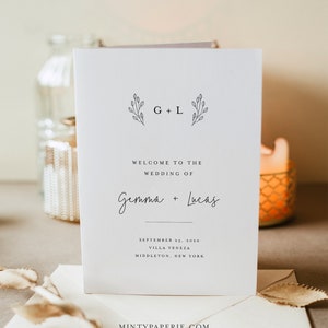 May include: A white wedding invitation card with a simple floral design and the text "G + L" at the top. The text "Welcome to the Wedding of Gemma + Lucas" is below the floral design. The date, location, and city are listed below the names. The text "MINTYPAPERIE.COM" is at the bottom of the card.