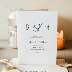 May include: Wedding ceremony program with the initials R&M in a simple script font with a small leaf design. The text reads "Welcome to the wedding ceremony of Rachel & Matthew, August 18, 2019, Villa Veneza, Middletown, New York."