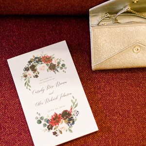 May include: A white wedding program with a floral wreath design in shades of red, pink, blue, and green. The text reads "Welcome to the wedding of Cassidy Rose Brown and Alex Richard Johnson June 23, 2019".