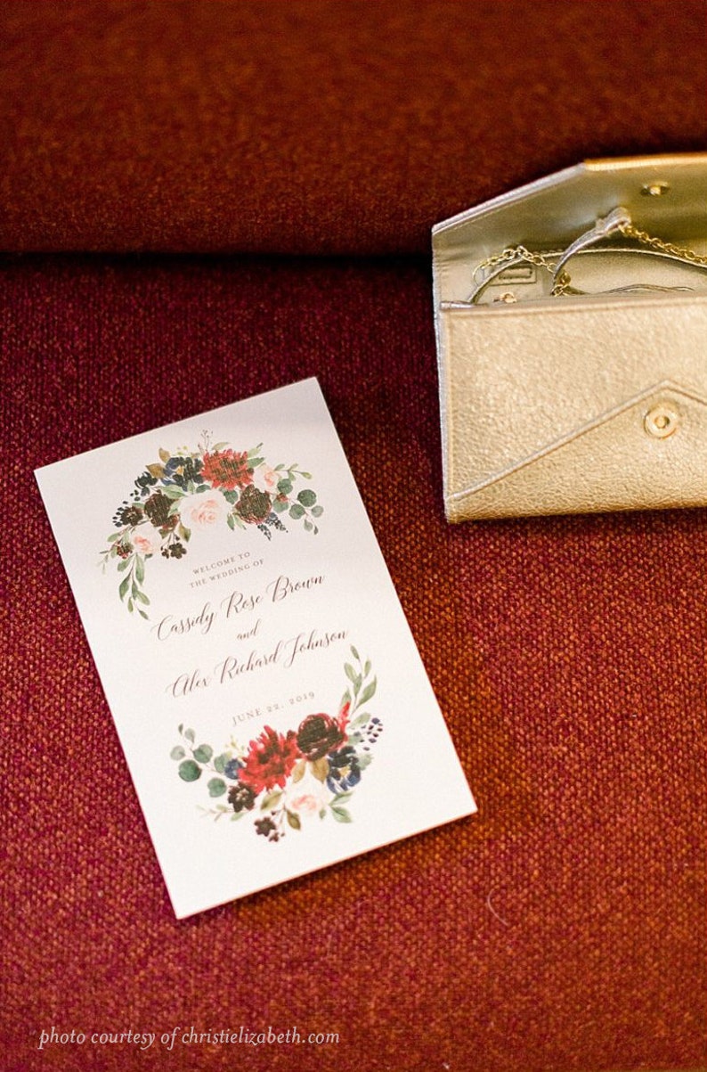 May include: A white wedding program with a floral wreath design in shades of red, pink, blue, and green. The text reads "Welcome to the wedding of Cassidy Rose Brown and Alex Richard Johnson June 23, 2019".