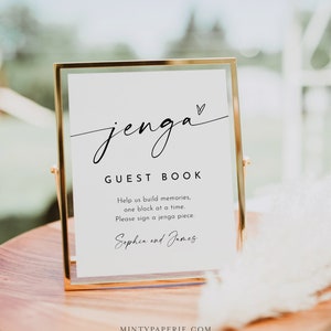 Könnte beinhalten: Ein weißes Schild in einem goldenen Rahmen mit dem Text "jenga GUEST BOOK" und der Nachricht "Helft uns, Erinnerungen zu schaffen, ein Block nach dem anderen. Bitte unterschreibt ein Jenga-Teil." Das Schild enthält auch die Namen "Sophia und James".