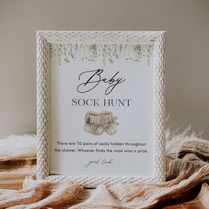 May include: A white framed sign with a floral border and the text "Baby Sock Hunt".  There are 10 pairs of socks hidden throughout the shower. Whoever finds the most wins a prize. Good luck.