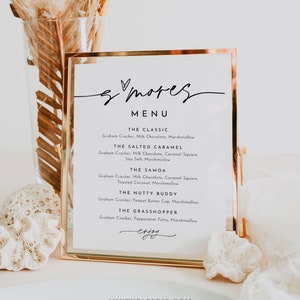 May include: A gold-framed menu sign with the word "smores" written in cursive script. The menu lists five different s'mores variations with ingredients, including "The Classic", "The Salted Caramel", "The Samoa", "The Nutty Buddy", and "The Grasshopper".
