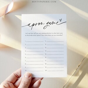 May include: A printable bridal shower game card with the title "apron game". The card has instructions to play the game, which involves remembering items on the bride-to-be's apron. There are 20 blank lines for guests to write down their answers.