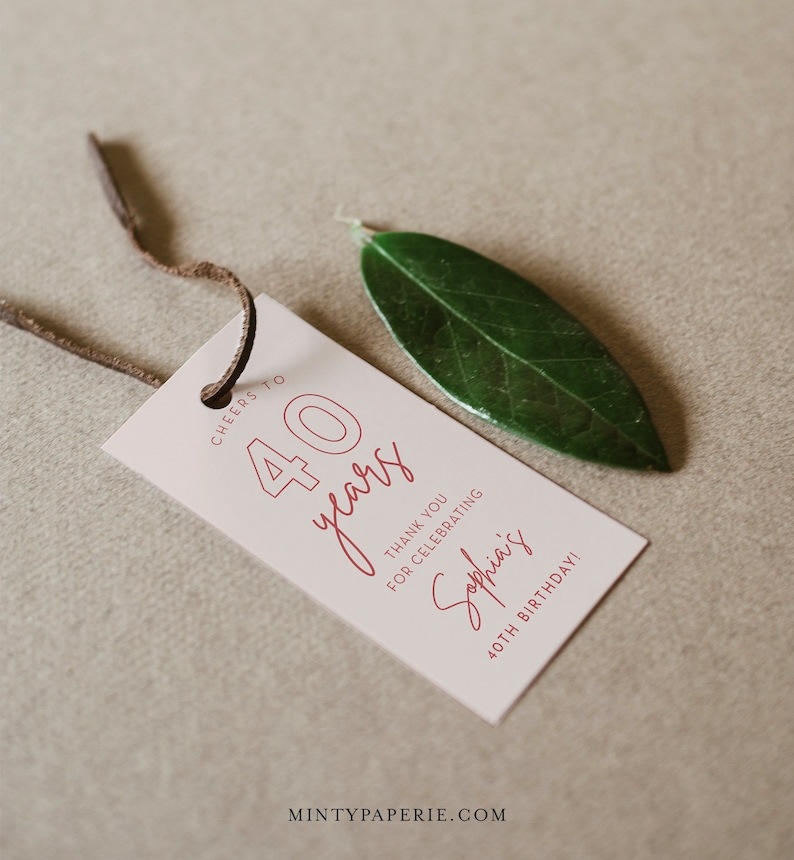 Puede incluir: Una etiqueta blanca con texto rojo que dice "Cheers to 40 years" y "Thank you for celebrating Sophia's 40th Birthday!" La etiqueta est&aacute; atada con un cord&oacute;n de cuero marr&oacute;n y una hoja verde est&aacute; sobre la etiqueta.