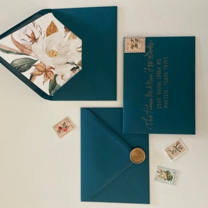 May include: Three teal blue envelopes with gold calligraphy. The envelope on the right has the address "The Future Mr. & Mrs. Foy Gordes 1500 Shoal Creek Rd. Austin, Texas 78751". The envelope on the left has a floral design inside.