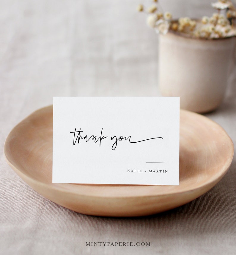 May include: White thank you card with black calligraphy that says "thank you" and the names "Katie - Martin" printed below.