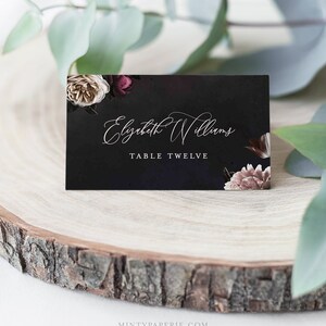 May include: Black wedding place card with white floral design and the text "Elizabeth Williams" and "Table Twelve".