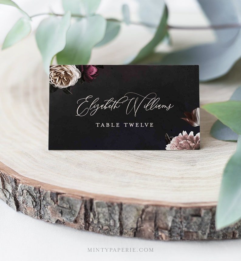 May include: Black wedding place card with white floral design and the text "Elizabeth Williams" and "Table Twelve".
