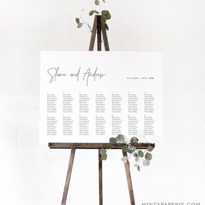 May include: A white wedding seating chart with the names "Shane and Andrew" written in black cursive at the top. The date "9.23.20XX" and the location "NEW YORK" are written in black below the names. The chart lists the names of guests assigned to each table number.