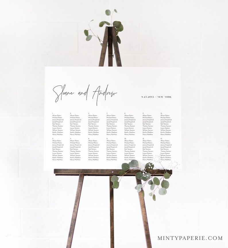 May include: A white wedding seating chart with the names "Shane and Andrew" written in black cursive at the top. The date "9.23.20XX" and the location "NEW YORK" are written in black below the names. The chart lists the names of guests assigned to each table number.